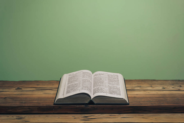 Otwórz Biblię na starym dębowym drewnianym stole. Zielona ściana w tle. - Zdjęcie, obraz