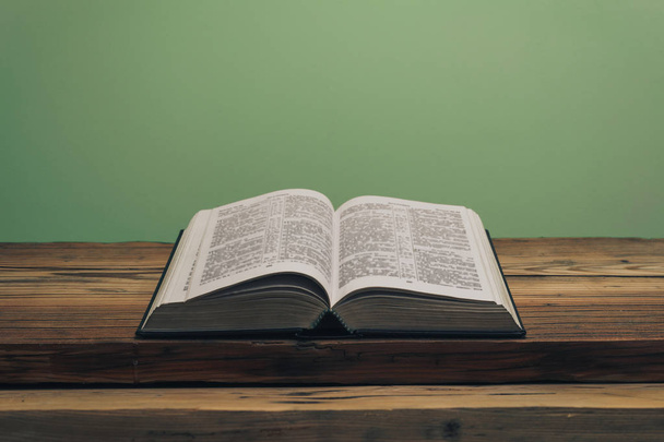 Kutsal İncil 'i eski bir meşe ağacından masanın üzerinde aç. Yeşil duvar arka planı. - Fotoğraf, Görsel