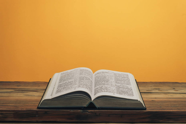 Apri la Sacra Bibbia su un vecchio tavolo in legno di quercia. Sfondo della parete arancione. - Foto, immagini