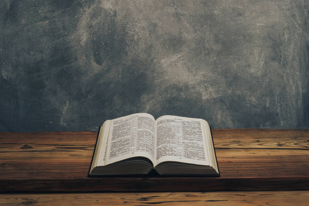 Відкрийте Святу Біблію на старому дерев'яному столі дуба. Поверхня стіни сірого кольору. - Фото, зображення