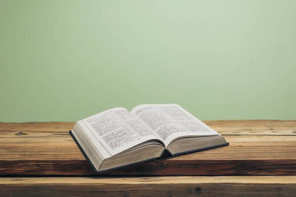 Откройте Библию на старом дубовом деревянном столе. Зеленый фон стены. - Фото, изображение