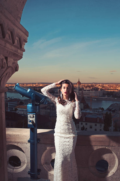Woman with telescope at viewpoint on cityscape. Woman with long hair in white wedding dress, fashion - Foto, Bild