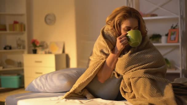 Ill female covered blanket drinking hot tea sitting on bed, health care, virus - Filmati, video