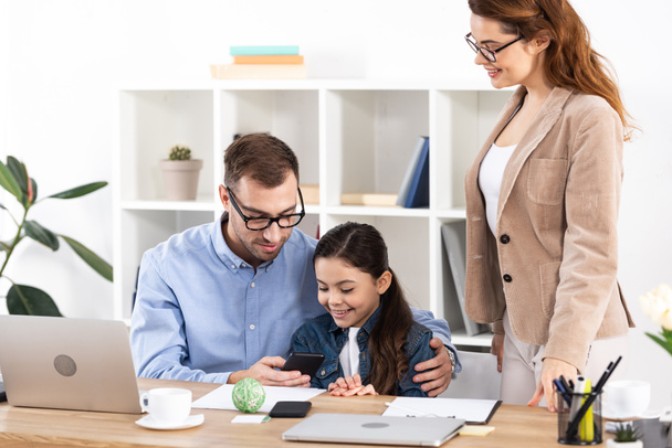 cheerful father using smartphone near happy daughter in office  - Photo, image