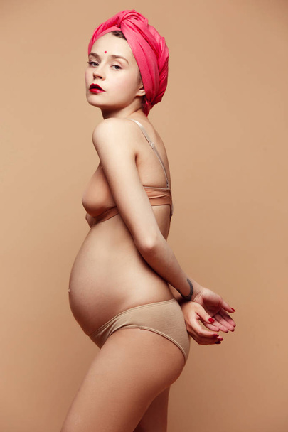 Young beautiful pregnant woman posing on brown background - Fotó, kép