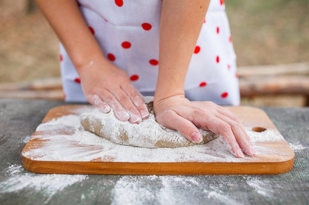 The girl in a white apron prepares the dough on a cutting board - Foto, imagen