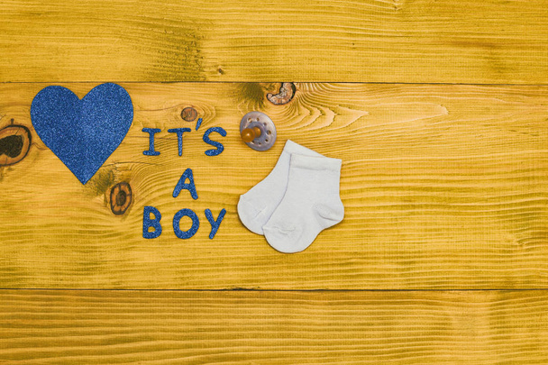 Text it's a boy with pacifier, little baby socks and heart shape on wooden table.Toned photo. - Foto, Bild