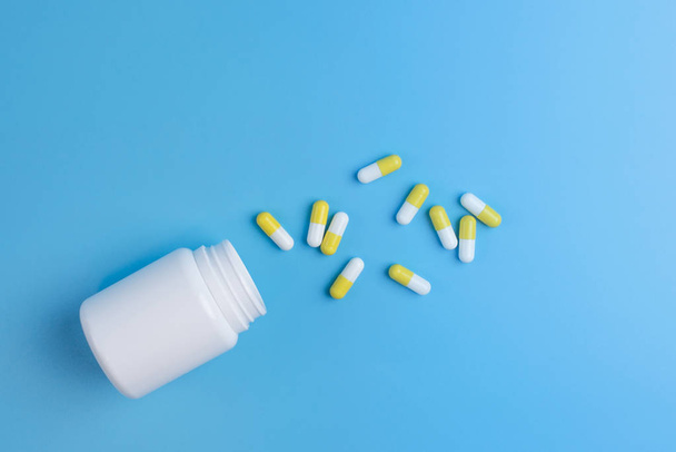 White and yellow pills, tablets and white bottle on blue backgro - 写真・画像
