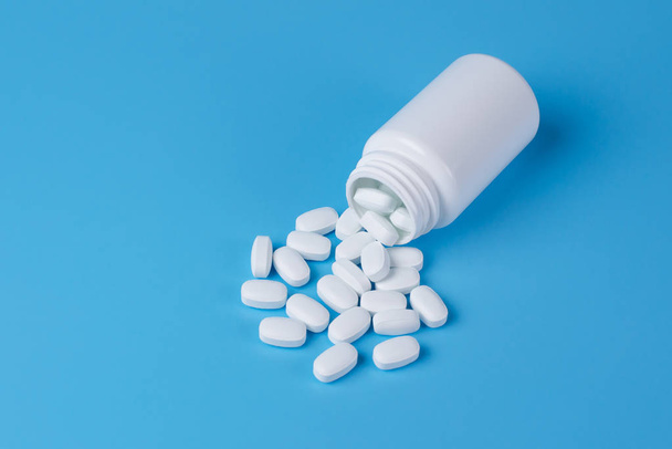 Witte pillen, tabletten en witte fles op blauwe achtergrond - Foto, afbeelding