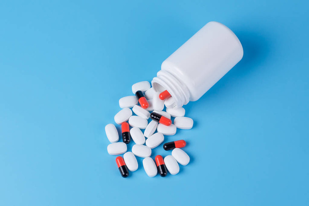 Oranje en zwarte pillen, tabletten en witte fles op blauw backgro - Foto, afbeelding