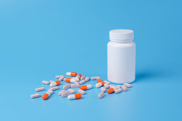 Oranžové a růžové tabletky, tablety a bílá láhev na modrý backgrou - Fotografie, Obrázek