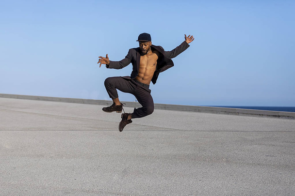 Front view young black man wearing casual clothes jumping in urban background. - Foto, immagini