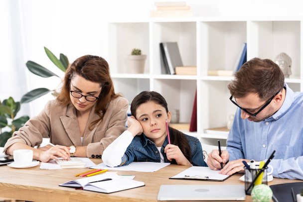 Trauriges Kind hält Bleistift neben Eltern in Brille im Büro  - Foto, Bild