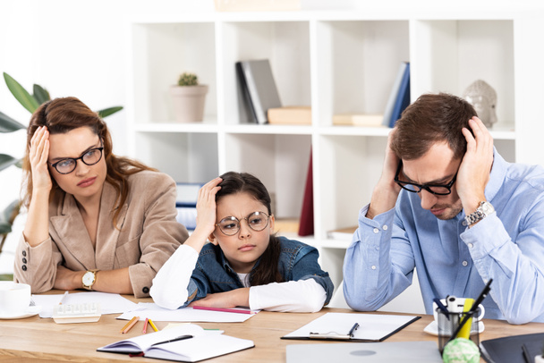 cute kid in glasses sitting with exhausted parents in office  - Фото, изображение