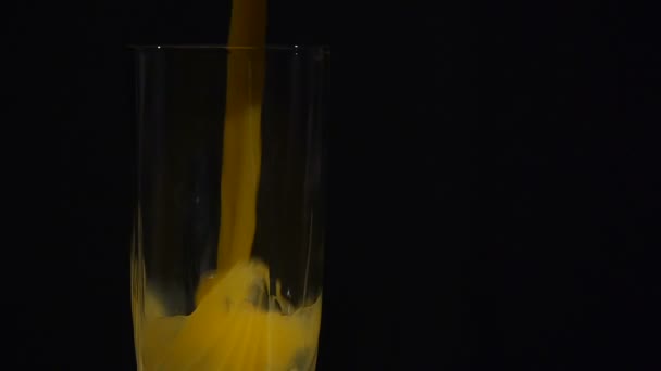 Gros plan. Le jus d’orange est versé dans un grand verre sur un fond noir. Jus d’orange ou d’ananas. - Séquence, vidéo
