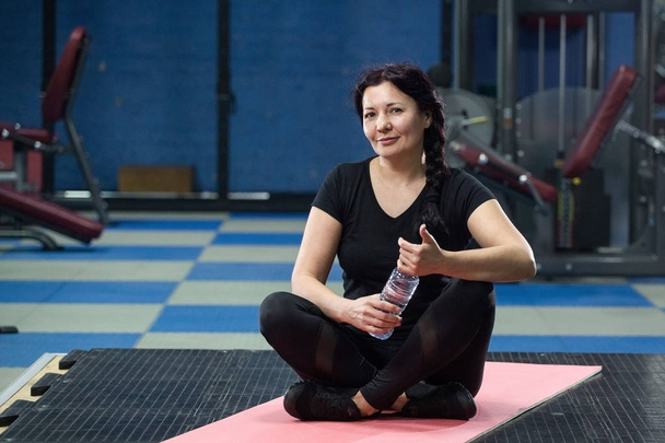 Senior woman in the gym sitting on a pink yoga mat. close-up. copy space. - Фото, изображение