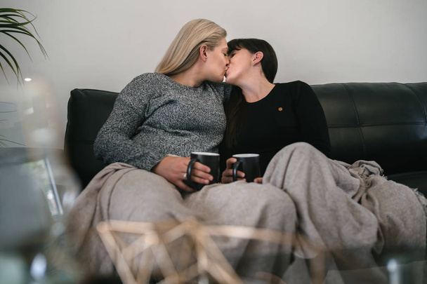 Young in Love Lesbische paar zittend op sofa en zoenen - Foto, afbeelding