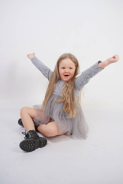 cute girl child with long blond hair sitting on the floor and yawns sweetly, stretching her hands in different directions on white studio background - Fotoğraf, Görsel