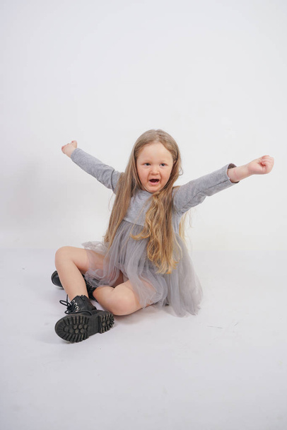 cute girl child with long blond hair sitting on the floor and yawns sweetly, stretching her hands in different directions on white studio background - Fotografie, Obrázek