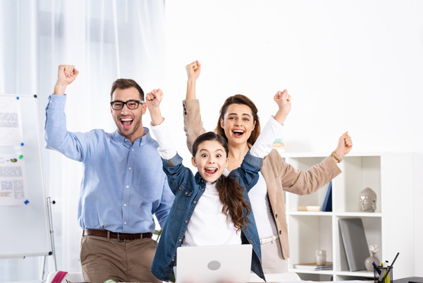 alegre familia celebrando triunfo cerca del portátil en la oficina
  - Foto, Imagen