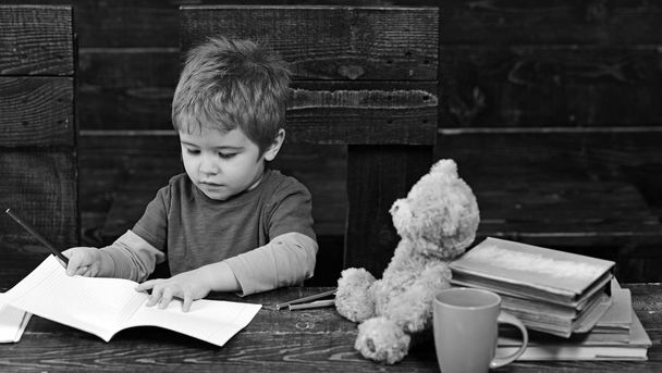 Concentrated kid writing in copybook. Preschool boy sitting at desk. Learning letters in kindergarten - Foto, imagen