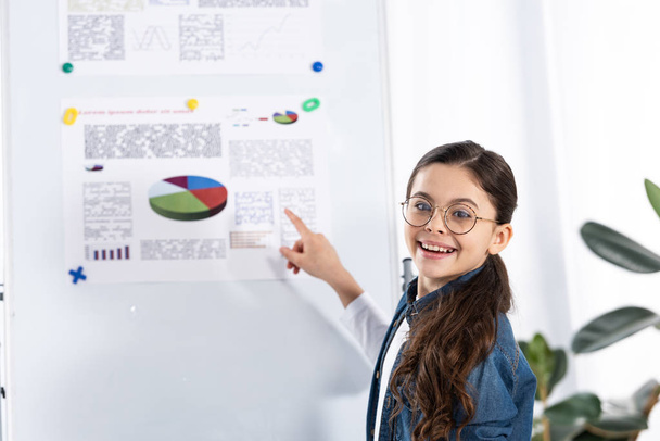happy kid in glasses pointing with finger at white board with charts and graphs  - Фото, изображение