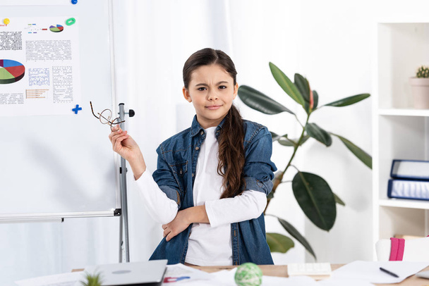 cute kid holding glasses while standing near white board in office  - Foto, Imagen