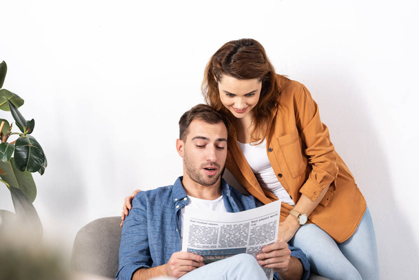 cheerful woman hugging man and reading newspaper at home  - Foto, imagen