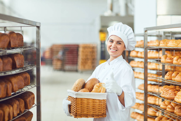A baker woman holding a basket of baked in her hands at the bakery - Fotoğraf, Görsel