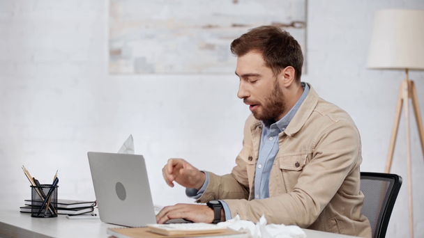  Brodaty biznesmen wpisując na laptopa, kaszel, kichanie i biorąc tkanek w biurze  - Materiał filmowy, wideo