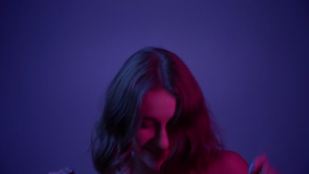 Closeup shoot of young pretty female dancing seductively in front of the camera with her hair fluttering with neon blue background - Imágenes, Vídeo