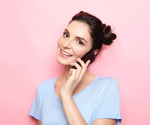 Teenage girl talking on a mobile phone over pink background - Foto, afbeelding