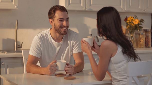 komea parrakas mies hymyilee, pitelee kuppia, juo kahvia ja puhuu brunette nainen keittiössä
  - Materiaali, video