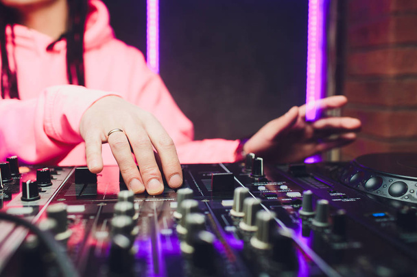 Close up view of the hands of male disc jockey mixing music on his deck with his hands poised over the vinyl record on the turntable and the control switches at night. - Foto, Imagem