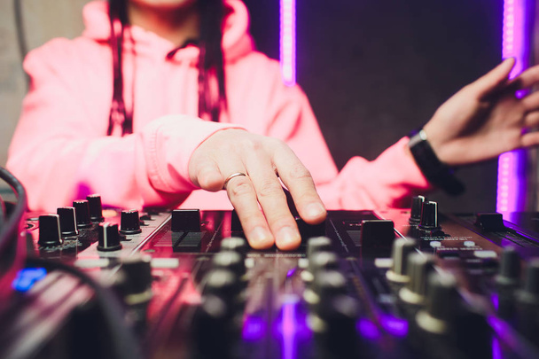 Close up view of the hands of male disc jockey mixing music on his deck with his hands poised over the vinyl record on the turntable and the control switches at night. - Foto, Imagem