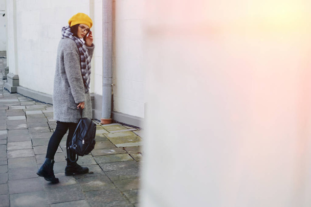 Привлекательная молодая девушка в очках в пальто и желтом берете вольная ходьба
 - Фото, изображение