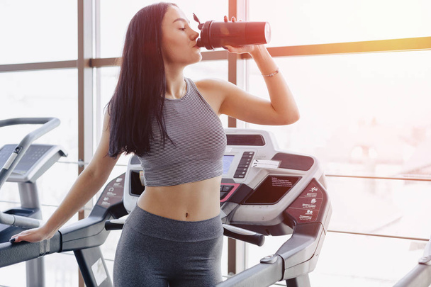 Girl in the gym are trained on treadmill and drink water - Foto, Imagem