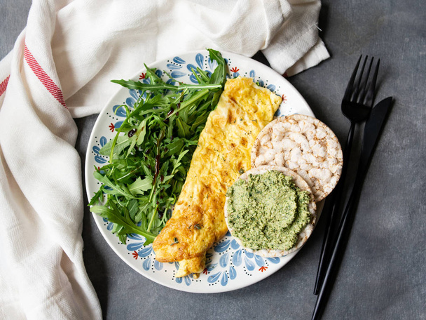 健康的な朝食-灰色の背景にペストとスクランブル卵、ルッコラとパン。完璧な卵は新鮮なルッコラとペストクラッカーとオムレツ。ベジタリアン料理だダイエット。選択的焦点、クローズアップ. - 写真・画像