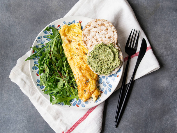 Healthy breakfast - scrambled eggs, arugula and bread with pesto on gray background. Perfect eggs omelette with fresh arugula and pesto cracker. Vegetarian food. Diet. Selective focus, close up. - Foto, immagini