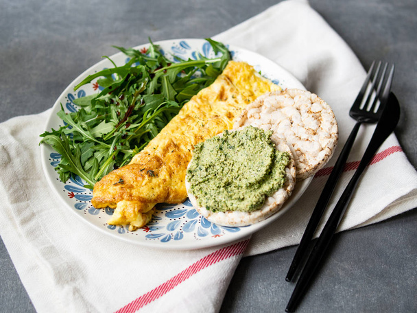 Healthy breakfast - scrambled eggs, arugula and bread with pesto on gray background. Perfect eggs omelette with fresh arugula and pesto cracker. Vegetarian food. Diet. Selective focus, close up. - 写真・画像