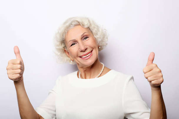 Elderly woman giving a thumb up and looking at the camera  - Foto, Bild