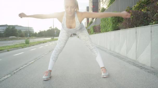 Close-up slow motion: actieve jonge vrouw die haar rug en benen rekt voordat ze gaat rennen. Onherkenbaar atletische vrouw die klaar is voor een pre-work JOG. Fit meisje training voor de jaarlijkse marathon - Video