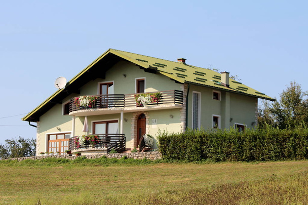 Belle nouvelle maison familiale de banlieue vert clair avec toit assorti et balcons en bois plein de fleurs entourées d'herbe et de haies sur fond de ciel bleu clair par une chaude journée ensoleillée
 - Photo, image