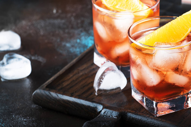 Trendy alcoholic cocktail Negroni with dry gin, red vermouth and red bitter, orange slice and ice cubes. Brown bar counter background, bar tools, night mood, copy space, selective focus - Foto, afbeelding