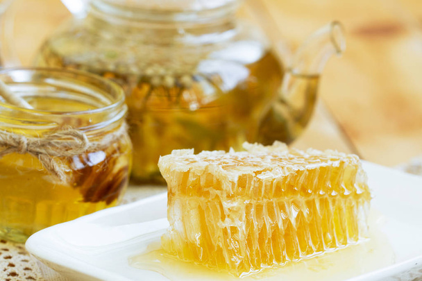 Honey comb piece. Honey slice with herbal tea and jar of honey on wooden table. honeycomb part with wax and liquid natural yellow honey. bee products by organic natural ingredients concept. rustic. - Foto, Bild