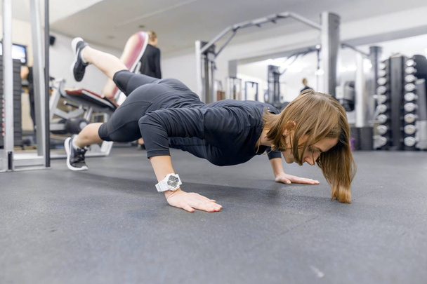 Young fitness woman working out doing push-ups on floor in sport gym. Sport, fitness, training, lifestyle and people concept - Valokuva, kuva