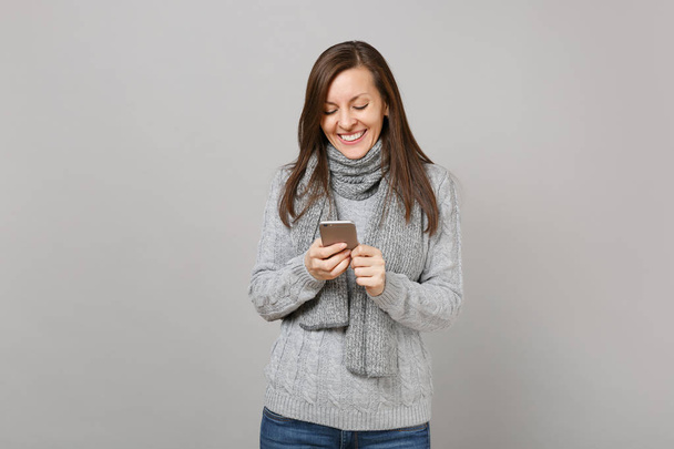 Uśmiechnięta młoda kobieta w szarym swetrze, szalik za pomocą telefonu komórkowego ty - Zdjęcie, obraz