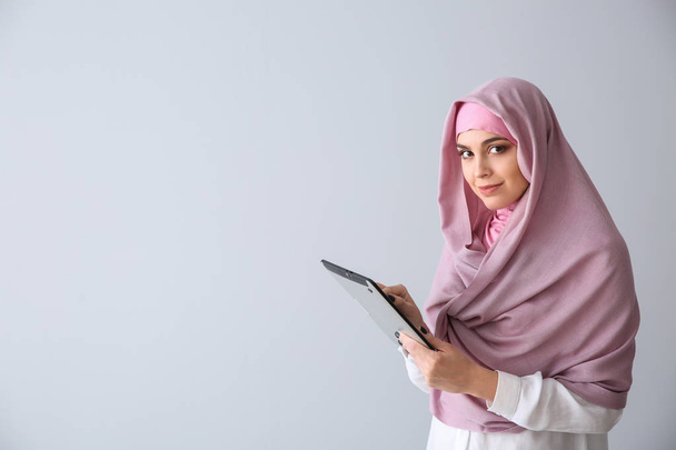 Young Muslim woman with tablet computer on light background - Foto, Imagem