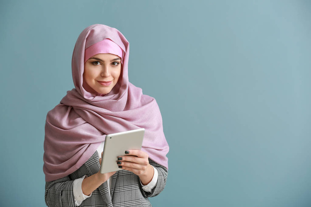 Young Muslim woman with tablet computer on color background - Valokuva, kuva
