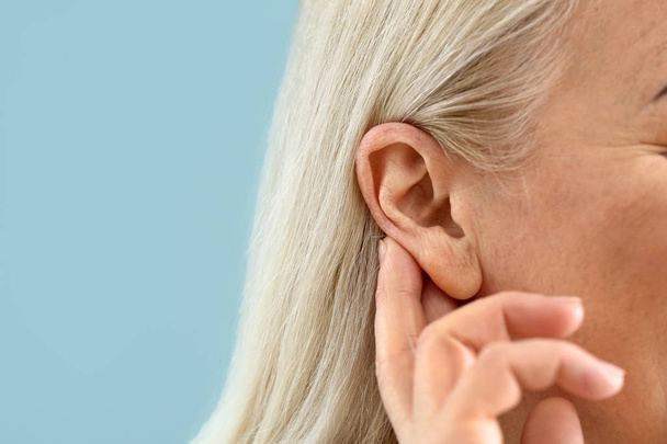 Mujer madura con problemas de audición en el fondo de color, primer plano
 - Foto, imagen